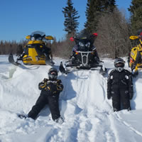 Two people in snowmobile suits laying against a snow bank. 