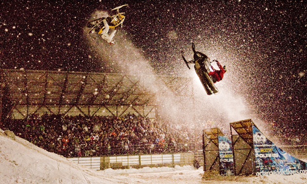 Two snowmobilers flipping through the air. 