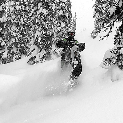 A snow biker plays in the trees. 