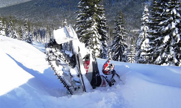 Photo of the back end of a snowmobile sticking out of the snow. 