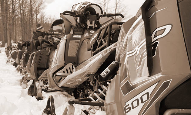 A black-and-white photo of a row of snowmobiles. 
