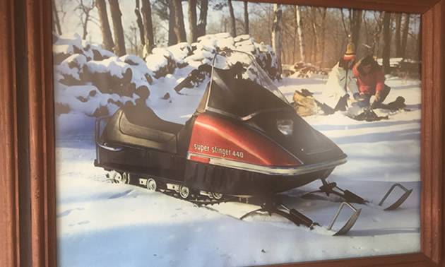 Back-lit barroom sign with a picture of a Scorpion snowmobile and couple sitting around a campfire. 