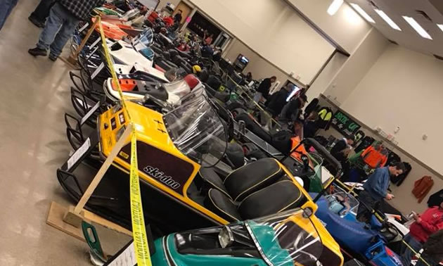 Line-up of snowmobiles in indoor arena. 