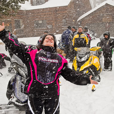 Snowmobiler throwing her hands up in joy at the snow falling. 