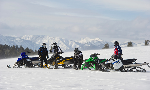 A group of snowmobilers sitting on top of a mountain. 