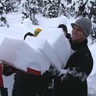 A man in a grey toque carrying some slabs of snow. 