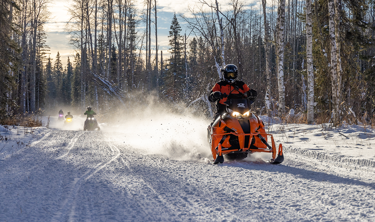 Several snowmobilers ride along a trail towards the camera