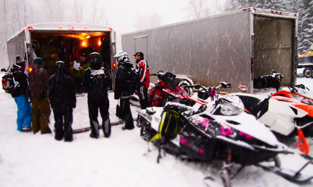 A group of snowmobilers discussing things at the trailer before they ride. 