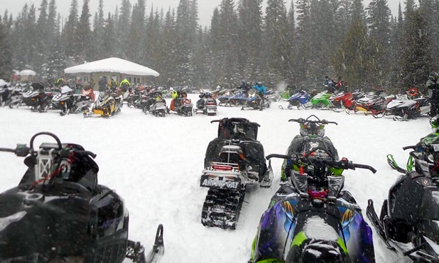 A large group of snowmobilers parked around the cabin. 