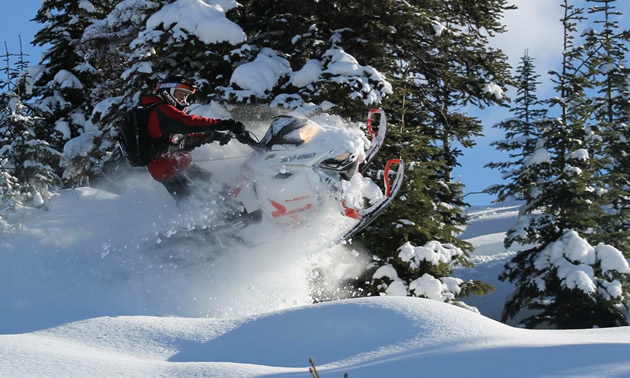 A snowmobiler on a white Ski-Doo busting through the pow. 