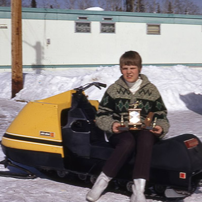 Picture of 13-year old Sue Thomas, sitting on snowmobile and holding trophy. 