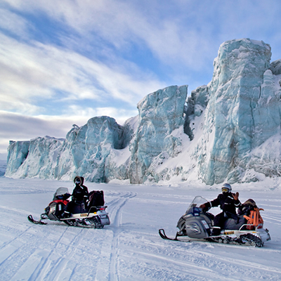 snowmobiles by a large mountains of ice in Norway. 