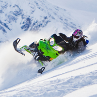 A woman on a green sled carving across a steep mountain. 
