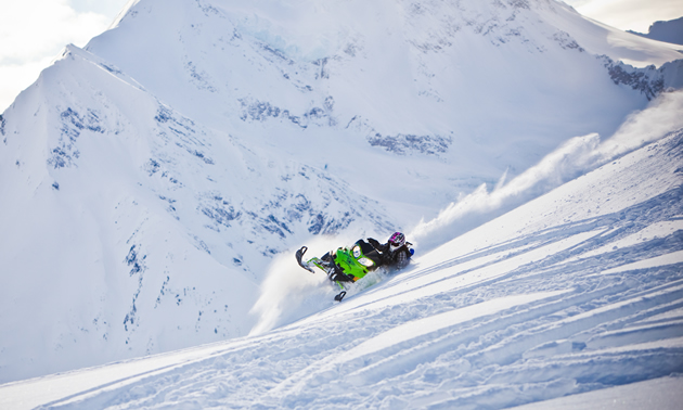 A woman on a green sled carving across a steep mountain. 