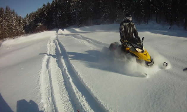 Photo of a guy riding a yellow sled through fresh powder. 