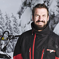 A man with blak hair and a mustache standing by a Polaris snowmobile. 