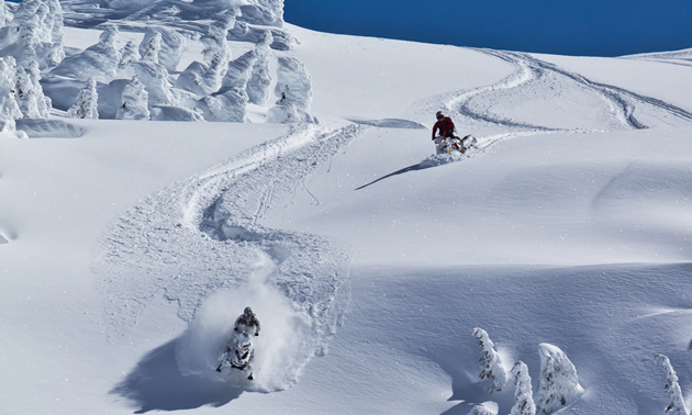 Two snowmobilers carving a line downhill in Whistler. 