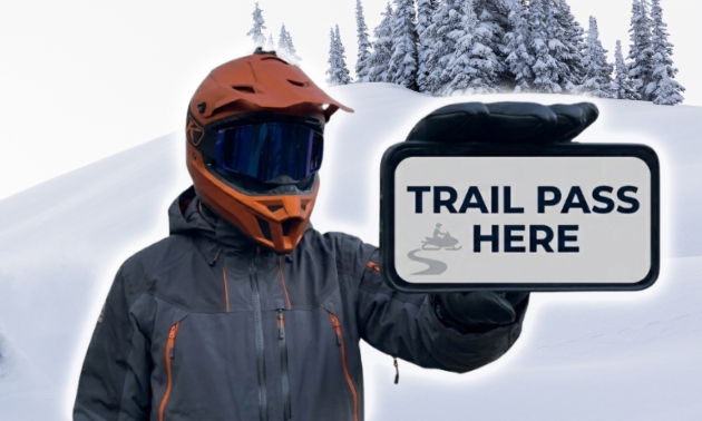 a snowmobiler holding a sign that says Trail pass Here