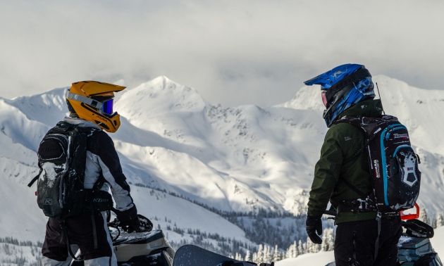 Two snowmobilers facing each other with snowy Valemount mountains in the background
