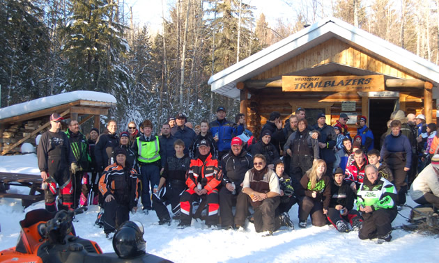 A group of snowmobilers standing in front of a cabin in Whitecourt. 