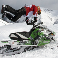 A woman doing a superman move on a parked snowmobile.