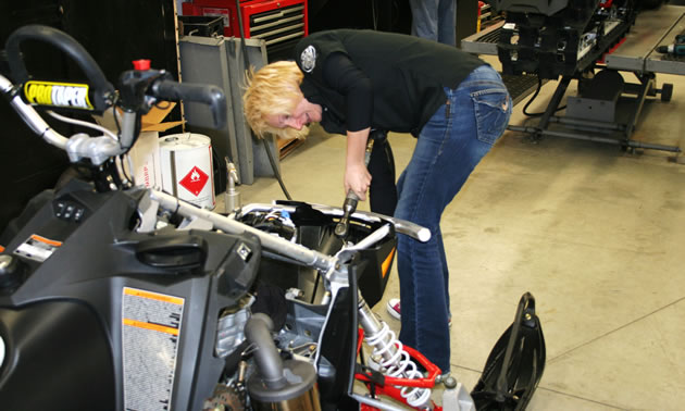 A blonde haired woman working on a snowmobile. 