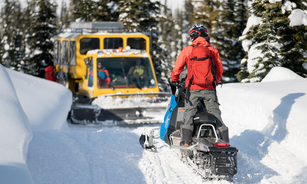 A snowmobiler is on a trail, facing a snowcat, and has no room to pass by.