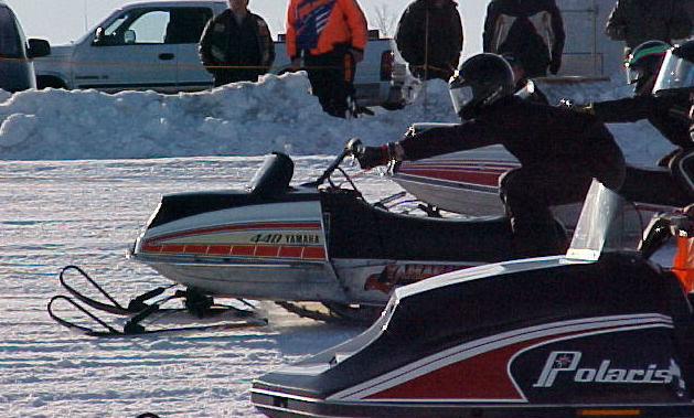 Two snowmobiles compete in an oval ice race.