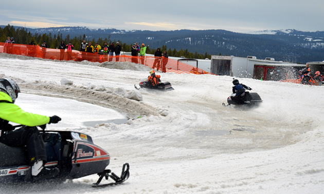 Vintage snowmobile oval racers round a turn at West Yellowstone. 