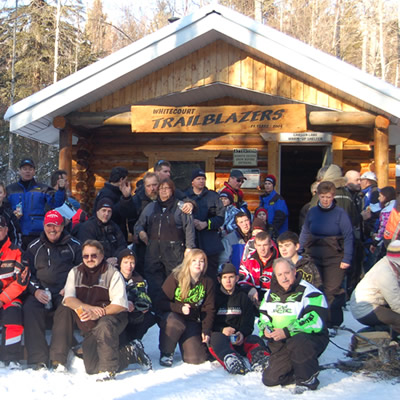 A big group of sledders gathered in front of a snowmobile cabin. 
