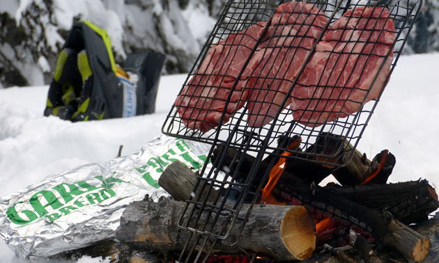 Three steaks roasting over a fire in the backcountry. 