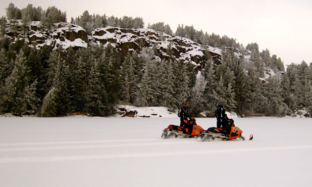 Two snowmobilers looking at a rocky outcropping. 