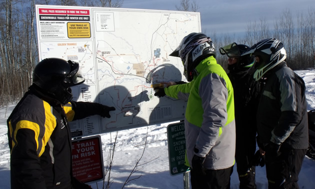 A group of snowmobilers looking at a billboard of snowmobile trail map in Whitecourt, Alberta. 