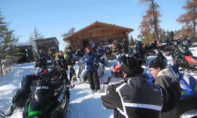 snowmobilers gathered in front of a cabin